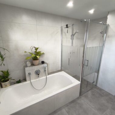 Großzügiges Badezimmer mit Badewanne, Glasdusche und hellen Wandfliesen.
