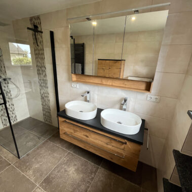 Modernes Badezimmer mit Doppelwaschtisch, Glasdusche und Holzoptik-Möbeln.