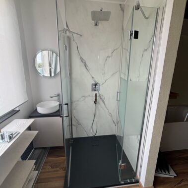 Modernes Badezimmer mit Aufsatzwaschbecken, bodengleicher Dusche und Marmoroptik-Fliesen.