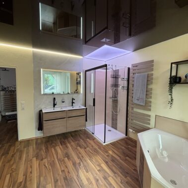 Großzügiges Badezimmer mit Badewanne, moderner Glasdusche, Doppelwaschtisch, indirekter Beleuchtung und Holzoptik-Bodenbelag.