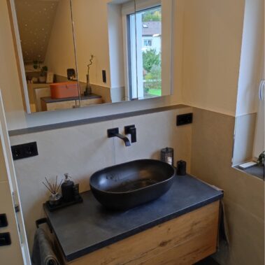 Modernes Badezimmer mit schwarzem Aufsatzwaschbecken, Holzunterschrank und Wandarmatur.