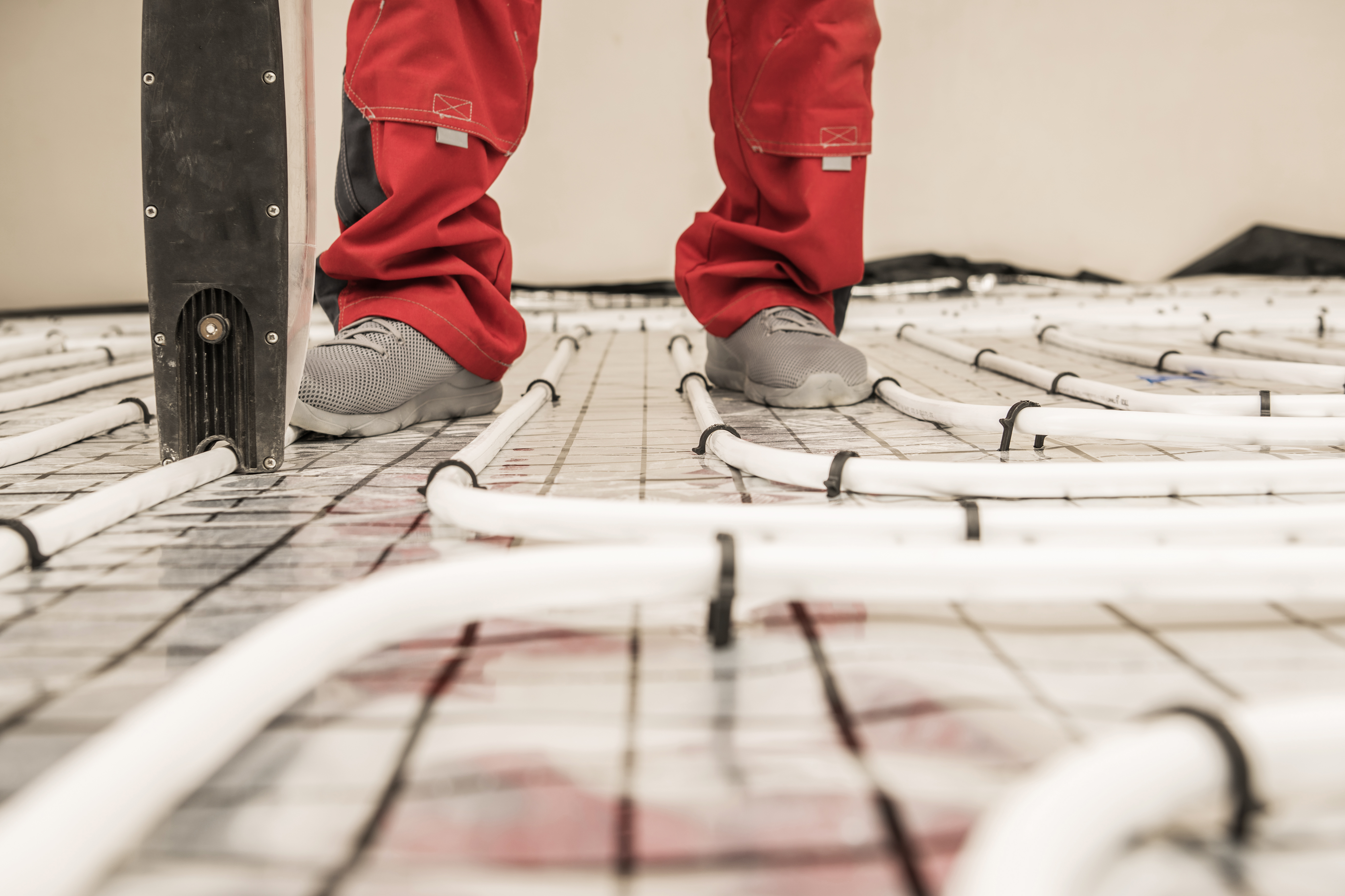 Handwerker bei der Verlegung einer modernen Fußbodenheizung mit Heizrohren auf einer Trägermatte vor dem Estricheinbau.